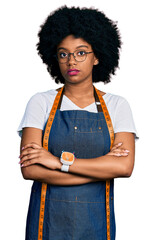 Poster - Young african american woman dressmaker designer wearing atelier apron relaxed with serious expression on face. simple and natural looking at the camera.