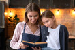 Portrait of cutie little girl and her beautiful young mother reading recipe book while baking cooking together at the kitchen. Attractive caucasian woman looking in book with daughter