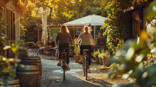 A Photo Of Two Women Riding Bicycles In Berlin, Back View, On A Sunny Day, With Green Trees And Plants Around Them, On A Street With An Outdoor Cafe, With A Nearby Wooden Barrel, A White Umbrella, In 