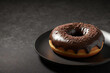 Chocolate donut on a black plate, on a dark background.