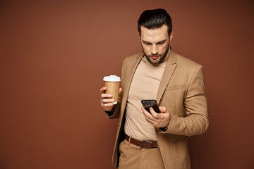 man in stylish attire holding coffee to go and using his smartphone on beige background, digital