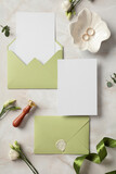 Fototapeta Mapy - Wedding invitation cards mockups with olive envelopes, gold rings, flowers, wax seal stamp on stone background. Flat lay, top view, copy space