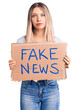 © Krakenimages.com - Young beautiful blonde woman holding fake news banner thinking attitude and sober expression looking self confident