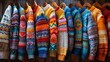 A vibrant display of handmade knit sweaters, each adorned with unique patterns and a spectrum of colors, hanging on wooden hangers.