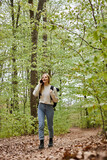 Fototapeta Zwierzęta - Pretty blonde woman traveler with backpack talking by phone walking in forest scenery
