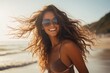 Smiling young beautiful woman with a bikini, wearing sunglasses on the beach, flowing hair, enjoying her summer vacation holiday travel