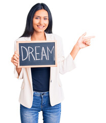 Wall Mural - Young beautiful latin girl holding blackboard with dream word smiling happy pointing with hand and finger to the side