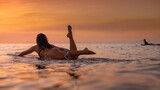 Fototapeta Miasta - Candid view of a woman surfer heading out to catch waves at sunset