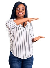 Wall Mural - Young african american woman wearing casual clothes and glasses gesturing with hands showing big and large size sign, measure symbol. smiling looking at the camera. measuring concept.