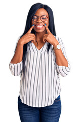 Sticker - Young african american woman wearing casual clothes and glasses smiling with open mouth, fingers pointing and forcing cheerful smile