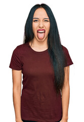 Wall Mural - Young hispanic girl wearing casual t shirt sticking tongue out happy with funny expression. emotion concept.