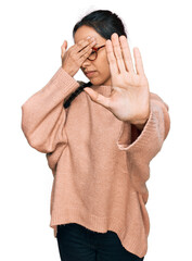 Wall Mural - Young hispanic girl wearing casual clothes and glasses covering eyes with hands and doing stop gesture with sad and fear expression. embarrassed and negative concept.