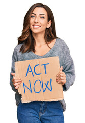 Wall Mural - Young brunette woman holding act now banner looking positive and happy standing and smiling with a confident smile showing teeth