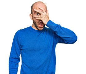 Poster - Young hispanic man wearing casual clothes peeking in shock covering face and eyes with hand, looking through fingers with embarrassed expression.