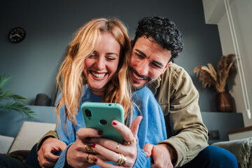 Young caucasian couple smiling using a cellphone to do shopping online. Man and woman watching the social media with a smartphone. Adult friends having fun browsing on internet with a mobile phone