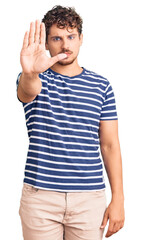 Wall Mural - Young handsome man with curly hair wearing casual clothes doing stop sing with palm of the hand. warning expression with negative and serious gesture on the face.