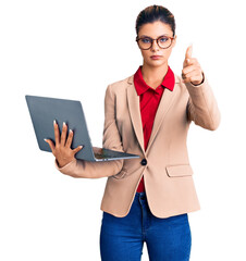 Sticker - Young beautiful woman holding laptop pointing with finger to the camera and to you, confident gesture looking serious