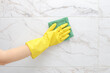 © Kristina - crop of female hand in yellow rubber glove cleaning a white marble ceramic tiles on the wall in the bathroom. Spring general or regular cleaning concept.