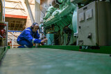 Fototapeta Do pokoju - Engineer in blue overall doing service of generator in Engine room of vessel. Work at sea.  Motorman.