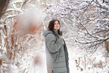 Fototapeta Koty - pretty woman in winter clothes among trees covered with snow, girl walking in snowy forest enjoying beautiful nature