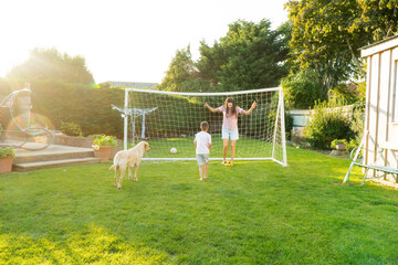 Young mother and son plays soccer with dog and have fun together. Happy family playing football with pet. Fun Playing Games in Backyard Lawn on Sunny Summer Day. Motherhood, childhood, togetherness