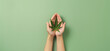 Hands holding green hemp marijuana leaf, pastel green background. Alternative treatment concept.