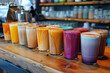 A variety of colorful specialty coffee drinks on a wooden counter. Row of shot glasses with colorful drinks on bar counter