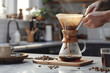 Person using a Chemex coffee maker to brew pour-over coffee . A person is pouring coffee into a chemex coffee maker