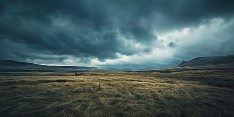 A field of grass with mountains under a dramatic grey sky in the background