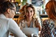 © Pinklife - Smiling young woman engaged in a discussion with her colleagues at a busy cafe, laptop in view