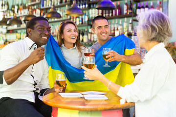 Wall Mural - Excited male and female football fans celebrating championship win, waving flag of Ukraine in beer pub