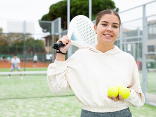 Wall Mural - Portrait of cheerful young female holding racket and ball in hands on padel court, outdoors