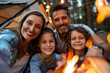 © mila103 - A family of four is sitting around a campfire, smiling
