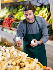 Wall Mural - Male salesman near fruit and vegetables stalls offering to buy garlic