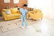 Cute African-American boy mopping floor in living room