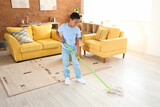 Fototapeta Mapy - Cute African-American boy mopping floor in living room
