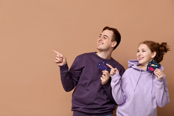 Poster - Young couple with credit cards pointing at something on brown background