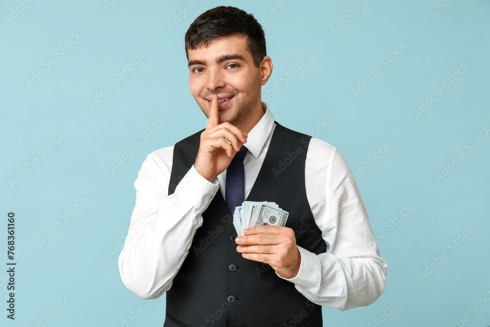 Young businessman with bribe showing silence gesture on blue background