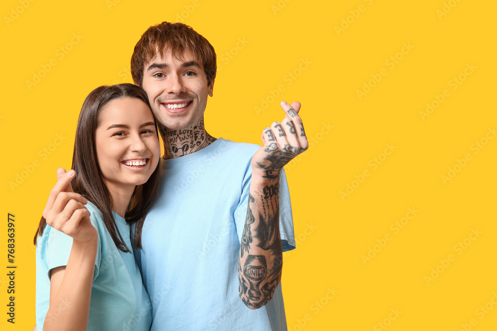 Young couple making hearts with fingers on yellow background