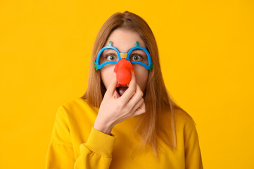 Wall Mural - Beautiful young shocked woman in funny disguise on yellow background. April Fools Day celebration