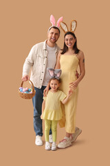 Wall Mural - Happy family in bunny ears holding basket with Easter eggs on beige background