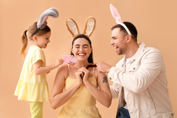 Wall Mural - Little girl with her father in Easter bunny ears tickle mother on beige background