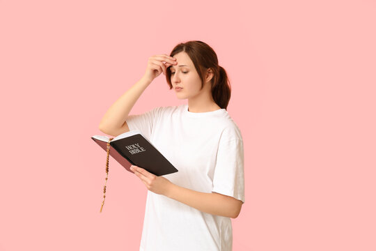 religious young woman with holy bible crossing herself on pink background