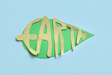 Paper word EARTH with green leaf on blue background. Earth Day celebration.