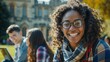 smiling student, glasses, curly hair, joyful, college campus, outdoor study, sunny day, historical architecture, youth, academic life, plaid scarf, casual wear, diverse group, leisure