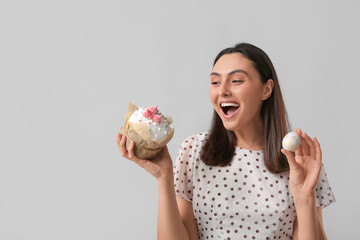 Canvas Print - Beautiful young woman with sweet Easter cake and egg on grey background