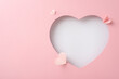 Mother's Day chic inspiration. Top view shot of delicate decorative hearts, showcased through a heart-shaped cutout on a pastel pink surface, offering space for heartfelt greetings or promotions