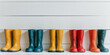 Row of rubber boots in solid colors lined against a white wall, ready for rainy day adventures.