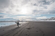 © Cavan Images - Woman walking on beach with surf board winter iceland