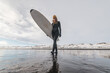 © Cavan Images - Woman walking on beach with surf board winter iceland